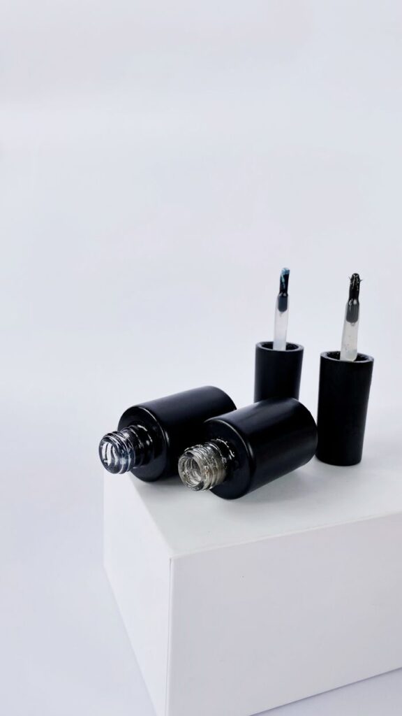 Minimalist display of black nail polish bottles with applicators on a white background, ideal for beauty and design themes.